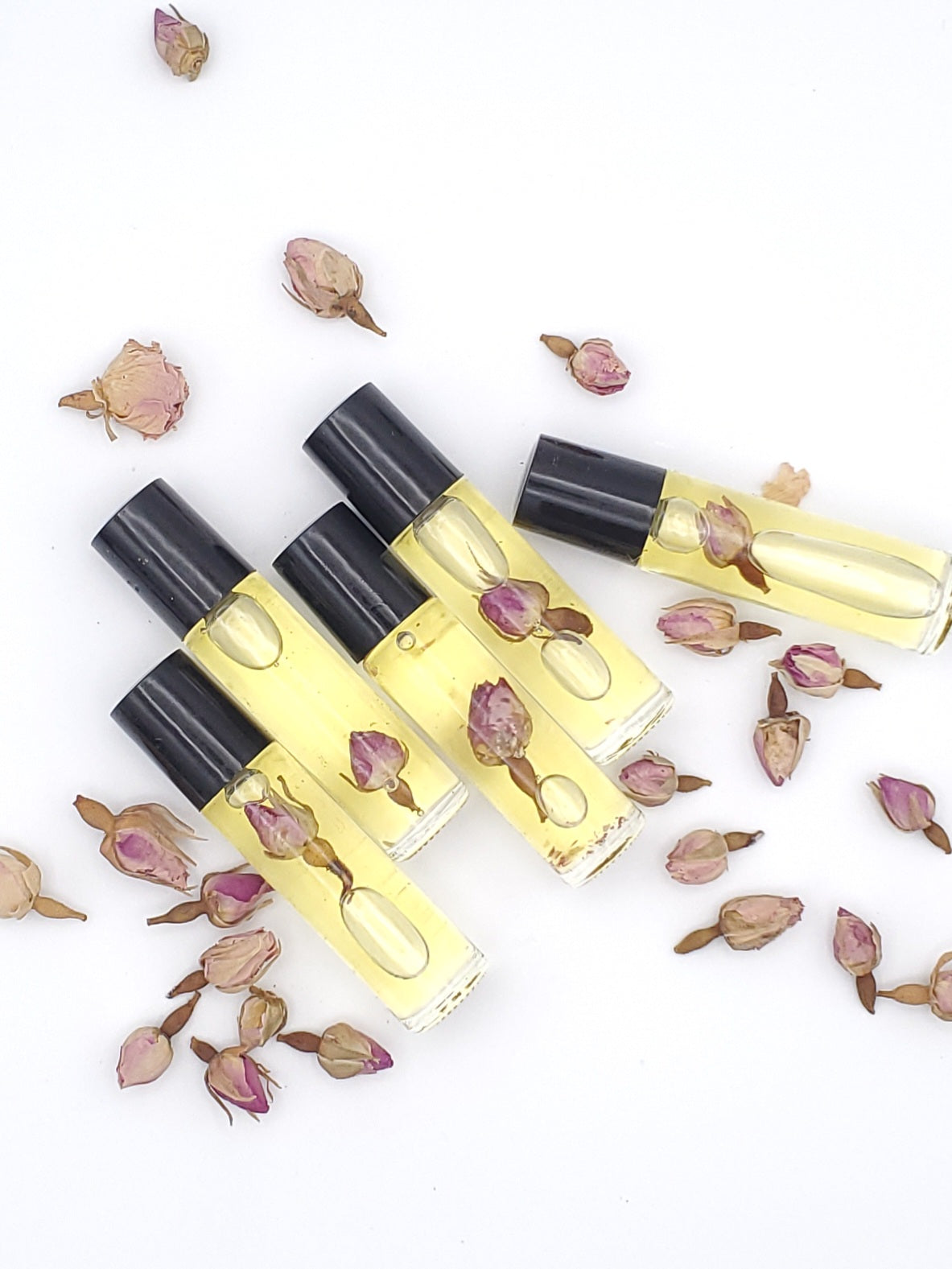 A clear glass bottle with a black cap, filled with yellow liquid, surrounded by rosehip seeds and petals on a white background.